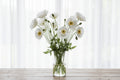 Bouquet of Bridal silk Poppy flowers in a clear vase on a wooden surface with a white curtain background