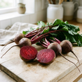 Fresh red beetroot with leafy tops and cut halves on a bright kitchen bench