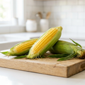 Golden sweet corn on a wooden chopping block in a bright white kitchen