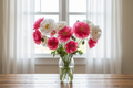 Papaver rhoeas Double Whoopee — large open double hot pink and white poppy blooms with golden centres in a clear glass vase in front of a window with white sheers