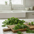 Fresh tender dark green baby spinach leaves spread on a rustic wooden board showing their delicate size, near a kitchen sink with silver tap