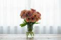 Strawberry Calendula blooms in a glass vase on a wooden table in front of white sheer curtains