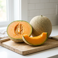 Netted cantaloupe melon with an orange-fleshed half and wedge on a pale board in a white kitchen