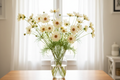 Cosmos bipinnatus Lemonade — soft creamy pale yellow single blooms with blush-pink centre and golden-yellow disc, with buds in a clear glass vase in front of a bright window