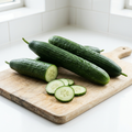 Whole green cucumbers and fresh cucumber slices on a pale wooden board in a bright white kitchen