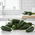 Plump glossy dark green jalapeño chillies with stems on a bright airy kitchen bench