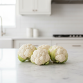 Three small compact white mini cauliflower heads grouped together on a bright airy kitchen bench