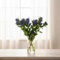 Gentiana makinoi Royal Blue stems in a glass vase on a wooden table in front of white sheer curtains